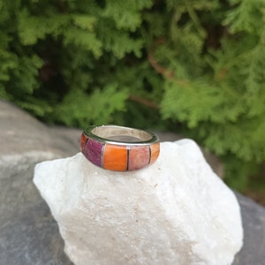May include: A silver ring with a multi-colored inlay of purple, orange, and pink stones.