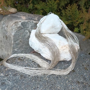 May include: A silver chain necklace with multiple strands, draped over a white rock. The necklace is made of thin, delicate chains.