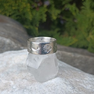 May include: A silver ring with a design of symbols and a small arrow on a white crystal.
