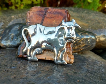 May include: A silver cow figurine with a detailed design. The figurine is standing on a piece of brown and orange agate.