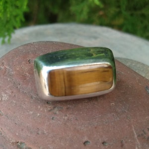 May include: A silver ring with a rectangular tiger's eye gemstone.