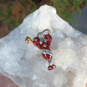 K&ouml;nnte beinhalten: Ein roter Hummer-Anh&auml;nger mit goldfarbenen Akzenten und dem Wort "MAINE" in Silber. Der Hummer hat eine silberfarbene Schlaufe zum Befestigen an einem Armband oder einer Halskette. Der Anh&auml;nger ist vor einem wei&szlig;en, kristallinen Hintergrund platziert.