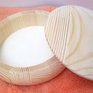 May include: A round wooden box with a lid. The box is made of light wood and has a natural finish. The lid is slightly domed and has a smooth surface.