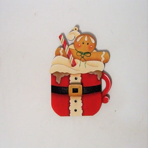 May include: A red and white Santa mug with a gingerbread man inside and a candy cane sticking out of the top. The mug has a black belt and white trim.