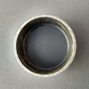 May include: A dark gray metal ring with a smooth, circular surface. The ring is about 2 inches in diameter.