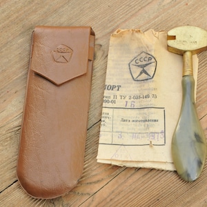 Könnte beinhalten: Ein Vintage-Glasschneider mit einem Messingkopf und einem grünen Kunststoffgriff. Der Glasschneider befindet sich in einem braunen Lederetui und wird mit einem Papieretikett geliefert, auf dem "СССР" und "ТУ 2-037-149-73" steht.