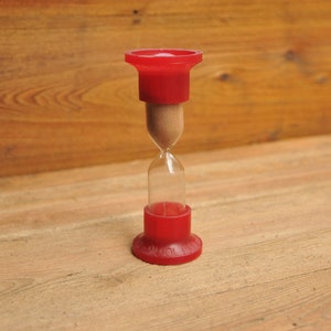 以下が含まれることがあります： ガラスの球体を通して砂が流れ落ちる赤い砂時計。砂時計はガラスとプラスチックでできています。