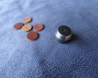 May include: Five round leather sanding discs in brown and tan colors, with a hole in the center of each disc. The discs are arranged in a cross shape. A silver metal sanding tool with a black top is on the right side of the image.
