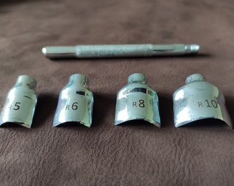 May include: Set of four silver metal tools for leather crafting. The tools are shaped like a curved blade and have different sizes marked R5, R6, R8, and R10. A silver metal handle is also included.