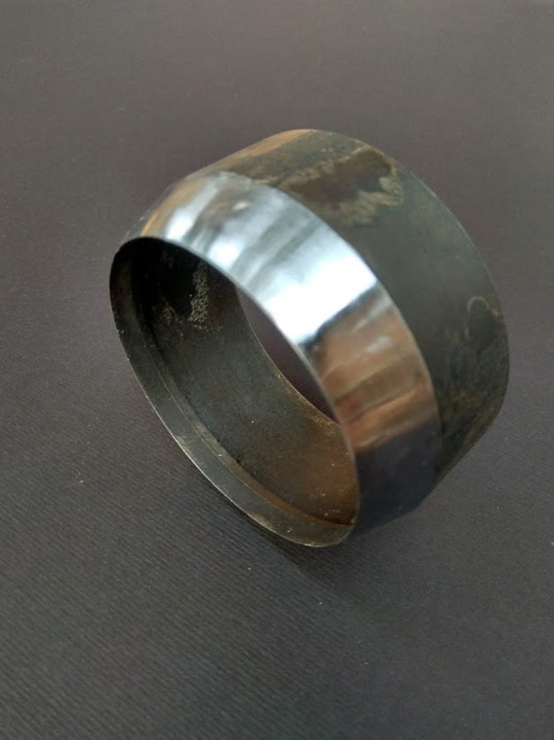 May include: A metal ring-shaped tool with a smooth, polished edge and a rough, textured surface. The tool is used for punching holes in leather or other materials.