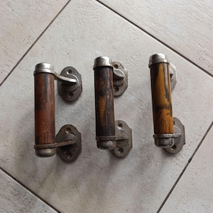 May include: Three antique door handles with wooden knobs and silver metal accents. The handles are mounted on a white tiled wall.