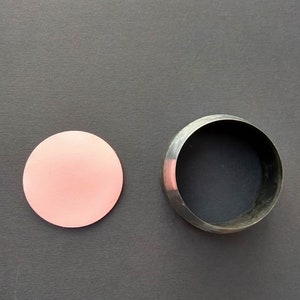 May include: A pink circle of craft paper next to a metal circle cookie cutter on a gray surface.