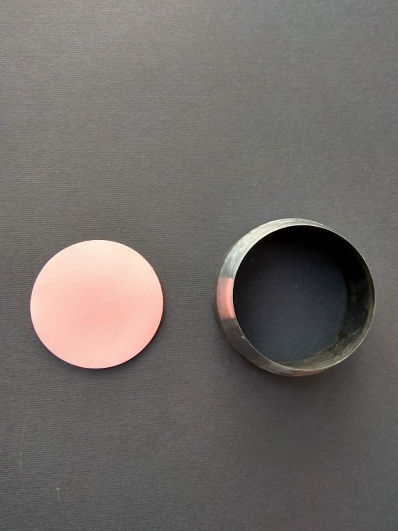 May include: A pink circle of craft paper next to a metal circle cookie cutter on a gray surface.