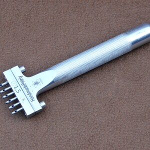 May include: Silver leather punch tool with a textured handle. The tool has six needles and is labelled "Handmade Petri 6/1.5".