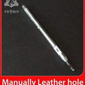 Puede incluir: Una herramienta de punzonado de cuero plateada con un mango negro y el número "2" impreso en el lateral. La herramienta está sobre un fondo negro.