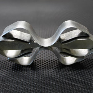 May include: A silver metal object with a unique, intricate design. The object is made of multiple pieces of metal that are bent and joined together to create a complex shape.