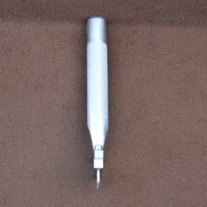 May include: A silver metal punch tool with a textured handle and a sharp point.