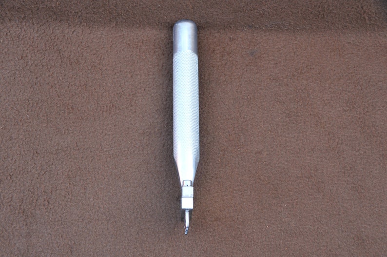 May include: A silver metal punch tool with a textured handle and a sharp point.