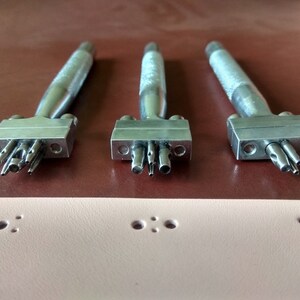 May include: Three silver leather hole punch tools with different sized punches. The tools are on a brown leather surface. The tools are used to create holes in leather for stitching or other purposes.
