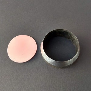 May include: A metal circle cutter with a pink leather punch out. The cutter is used to create circles in leather.