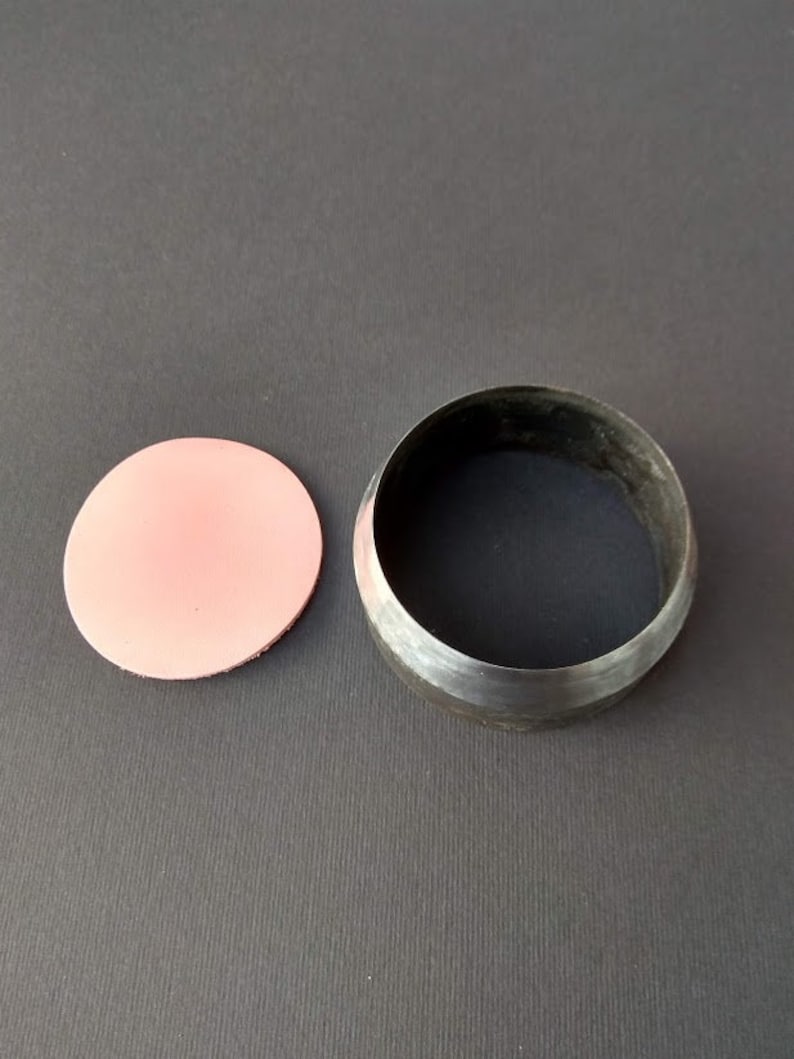 May include: A metal circle cutter with a pink leather punch out. The cutter is used to create circles in leather.