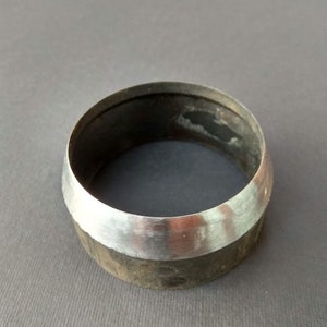 May include: A silver metal ring with a dark gray band. The ring is smooth and shiny.