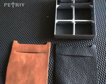 Könnte beinhalten: Zwei Leder-Taschen, eine braune und eine schwarze, mit einer Schablone aus Metallgitter. Die Schablone hat sechs quadratische Fächer.
