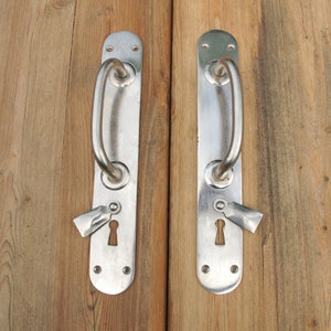 Puede incluir: Dos manillas de puerta plateadas con mirillas en una puerta de madera.