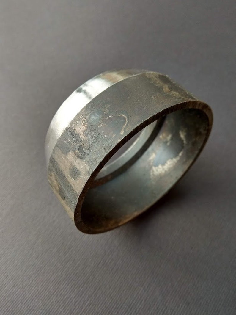 May include: A silver and black metal ring with a smooth, polished surface. The ring is made of two pieces of metal that are joined together.