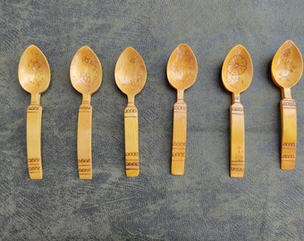 May include: Six wooden spoons with intricate floral designs carved into the bowl of each spoon. The spoons are all the same size and shape, and they are arranged in a row on a green surface.
