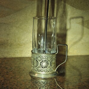 Puede incluir: Un portavasos de plata con un dise&ntilde;o intrincado. El portavasos est&aacute; dise&ntilde;ado para sostener un vaso alto con una pajita. El portavasos est&aacute; sobre una encimera de granito marr&oacute;n.