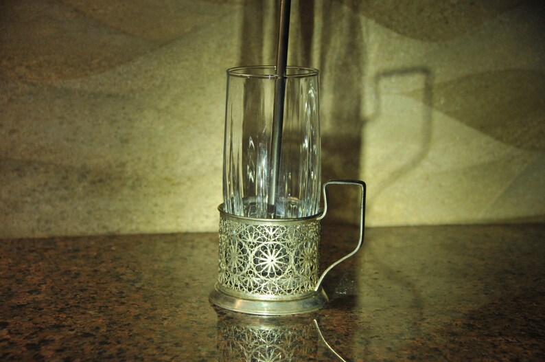 Puede incluir: Un portavasos de plata con un dise&ntilde;o intrincado. El portavasos est&aacute; dise&ntilde;ado para sostener un vaso alto con una pajita. El portavasos est&aacute; sobre una encimera de granito marr&oacute;n.