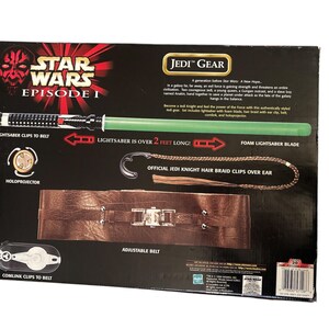 May include: Star Wars Episode I Jedi Gear playset with a green lightsaber, a brown belt with metal buckles, and a hair braid clip. The box features the text "Lightsaber is over 2 feet long!"