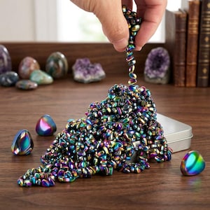 May include: A large collection of small, iridescent, rainbow-colored magnetic hematite stones. The stones are metallic with a reflective finish, showing hues of blue, purple, green, and gold. They are shaped like small, smooth, rounded pebbles.