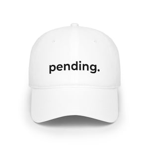 Könnte beinhalten: Eine weiße Baseballkappe mit gebogenem Schirm. Das Wort "pending." ist in Schwarz auf der Vorderseite aufgedruckt. Die Kappe hat eine strukturierte Passform und ein klassisches Design, geeignet für Freizeitkleidung.