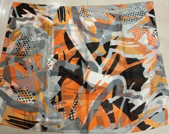 Op de afbeelding: Een dunne sjaal met een abstract print in tinten oranje, zwart en grijs. De print bevat geometrische vormen en stippen.