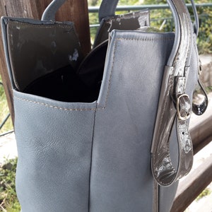 May include: A gray leather tote bag with a brown leather strap and buckle. The bag has a top flap with a magnetic closure.