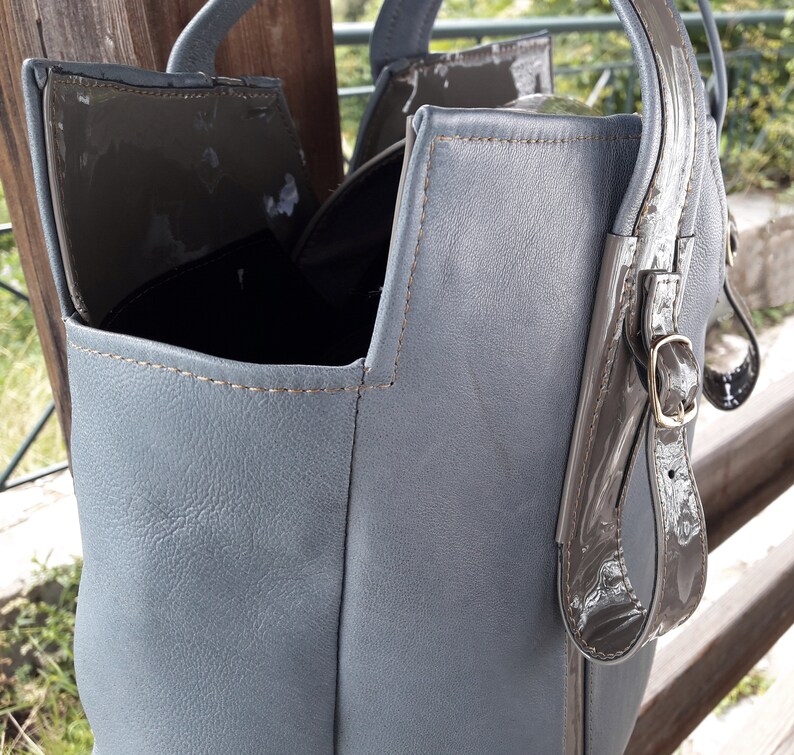 May include: A gray leather tote bag with a brown leather strap and buckle. The bag has a top flap with a magnetic closure.