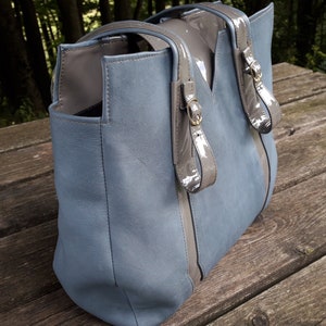 May include: A blue leather tote bag with gray leather accents and gold buckles. The bag has a top zipper closure and two top handles.