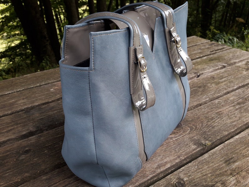 May include: A blue leather tote bag with gray leather accents and gold buckles. The bag has a top zipper closure and two top handles.