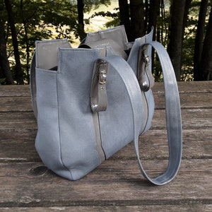 May include: A light blue tote bag with a long strap. The bag has a zipper closure and a contrasting gray stripe down the front.