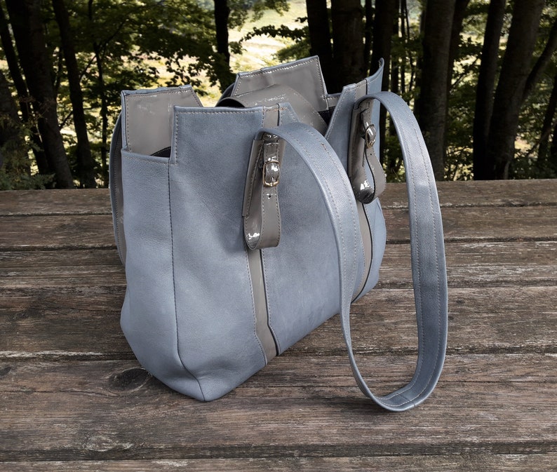 May include: A light blue tote bag with a long strap. The bag has a zipper closure and a contrasting gray stripe down the front.