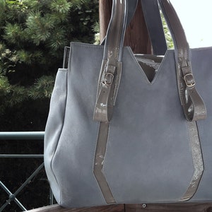 May include: A light blue leather tote bag with two brown leather straps and buckles. The bag has a V-shaped top and a large, open top.