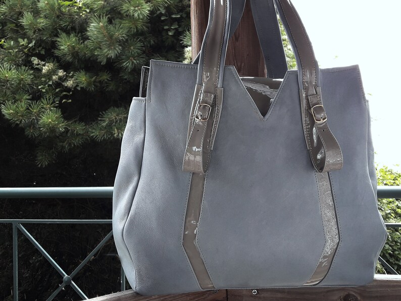 May include: A light blue leather tote bag with two brown leather straps and buckles. The bag has a V-shaped top and a large, open top.
