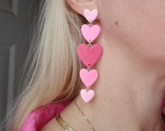May include: Pink and red heart shaped dangle earrings. The earrings are made of polymer clay and are strung on a silver chain.