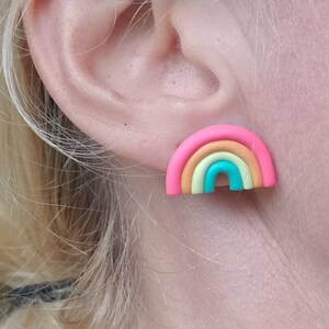 May include: A colorful rainbow stud earring. The earring features a pink outer band, followed by bands of yellow, orange, and turquoise. The earring is a small, cheerful accessory.