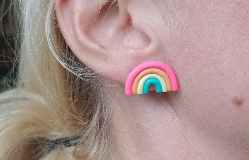 May include: A colorful rainbow stud earring. The earring features a pink outer band, followed by bands of yellow, orange, and turquoise. The earring is a small, cheerful accessory.
