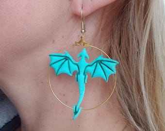May include: Teal dragon dangle earrings with gold hoop settings. The dragon is in flight with wings spread and a long tail.