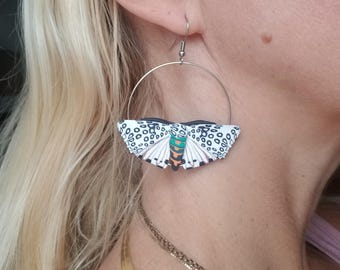 May include: A pair of hoop earrings with a white and black butterfly charm. The butterfly has green and orange accents.