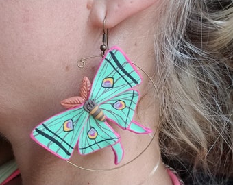 May include: A pair of hoop earrings with a green and pink butterfly charm. The butterfly has black stripes and yellow and purple accents.